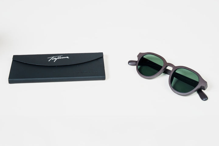 Tajima foldable sunglass case closed flat next to a pair of sunglasses with green polarized lenses